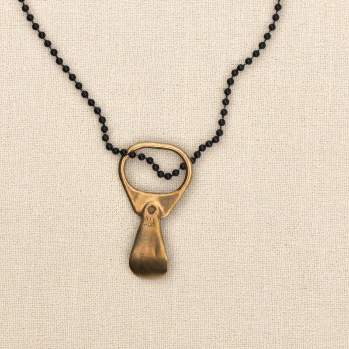 A necklace featuring the back of a solid bronze pop top pendant on a linen background